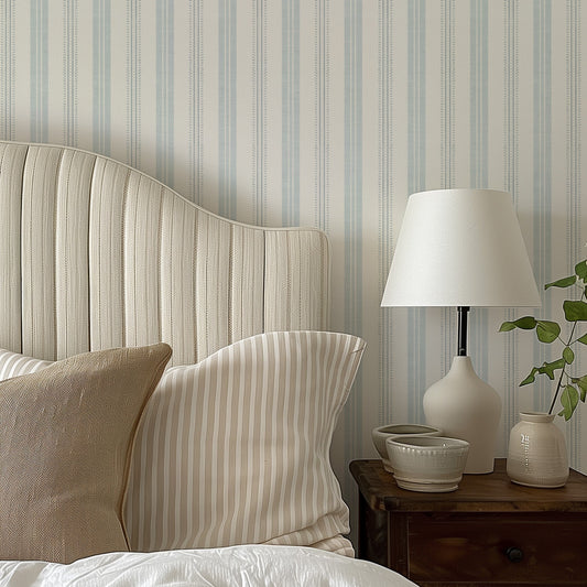 Antique Linen Stripe Wallpaper in Cream on Hinting Blue shown in a bedroom.