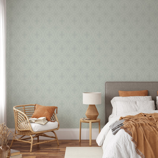 Bedroom with sage patterned wallpaper, wicker chair, and wooden nightstand.