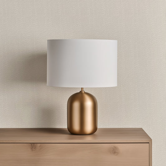 Table lamp with a gold base and white shade on a wooden surface against a wallpapered Freehand Dashes in Pashmina design.
