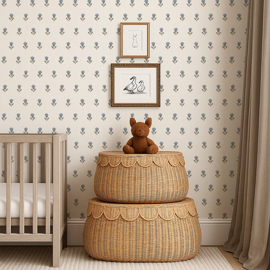 Nursery room with wicker ottomans, teddy bear, and framed pictures on patterned thistle buds wallpaper in blue.